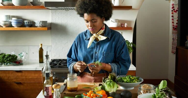 "A woman stands in a kitchen, chopping various healthy vegetables on a cutting board. She appears focused and engaged in the food preparation process."